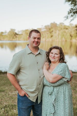 A couple poses by a lake during golden hour in casual attire.