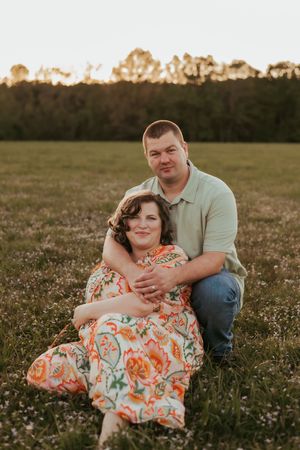 A couple sits together in a flowering field at sunset.