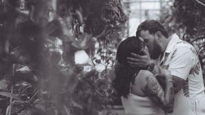 A black and white photo of a couple sharing a tender moment in a greenhouse setting.