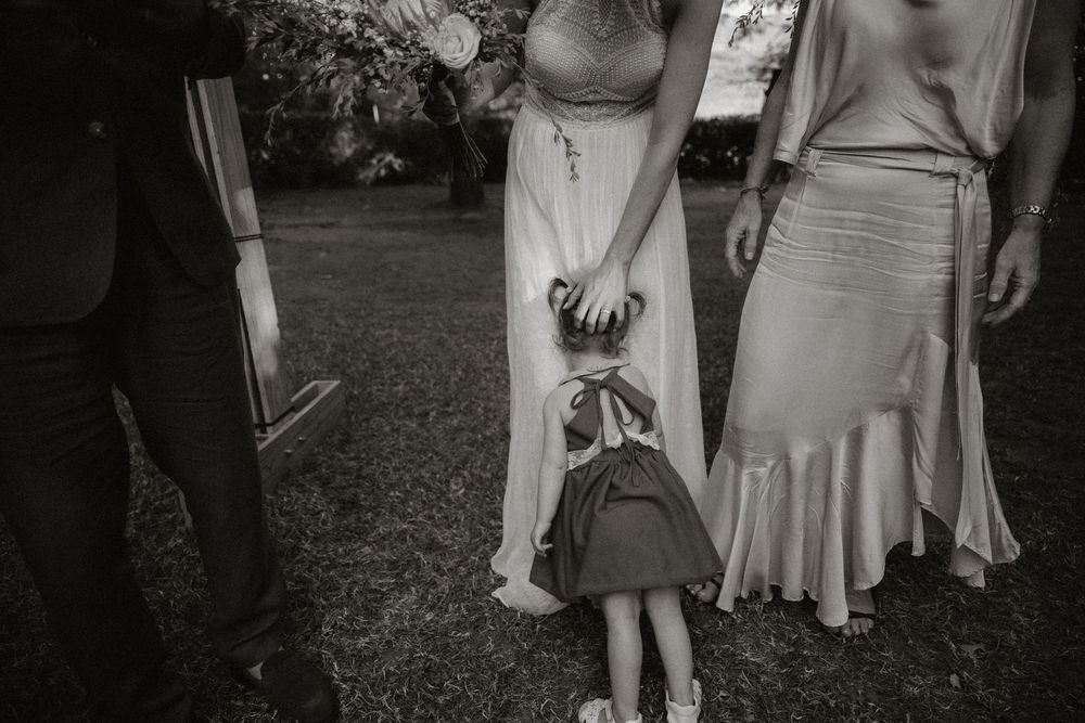 Black and white wedding photo of bride holding hands with flower girl in garden ceremony.