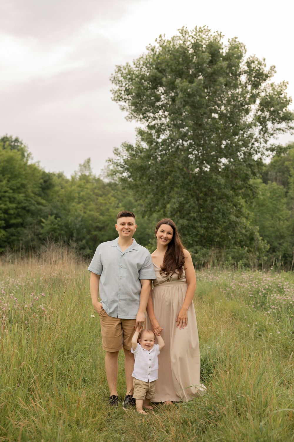A family stands together in a grassy meadow at Douglas Evan nature preserve in Michigan surrounded by tall green trees on a summer day.
