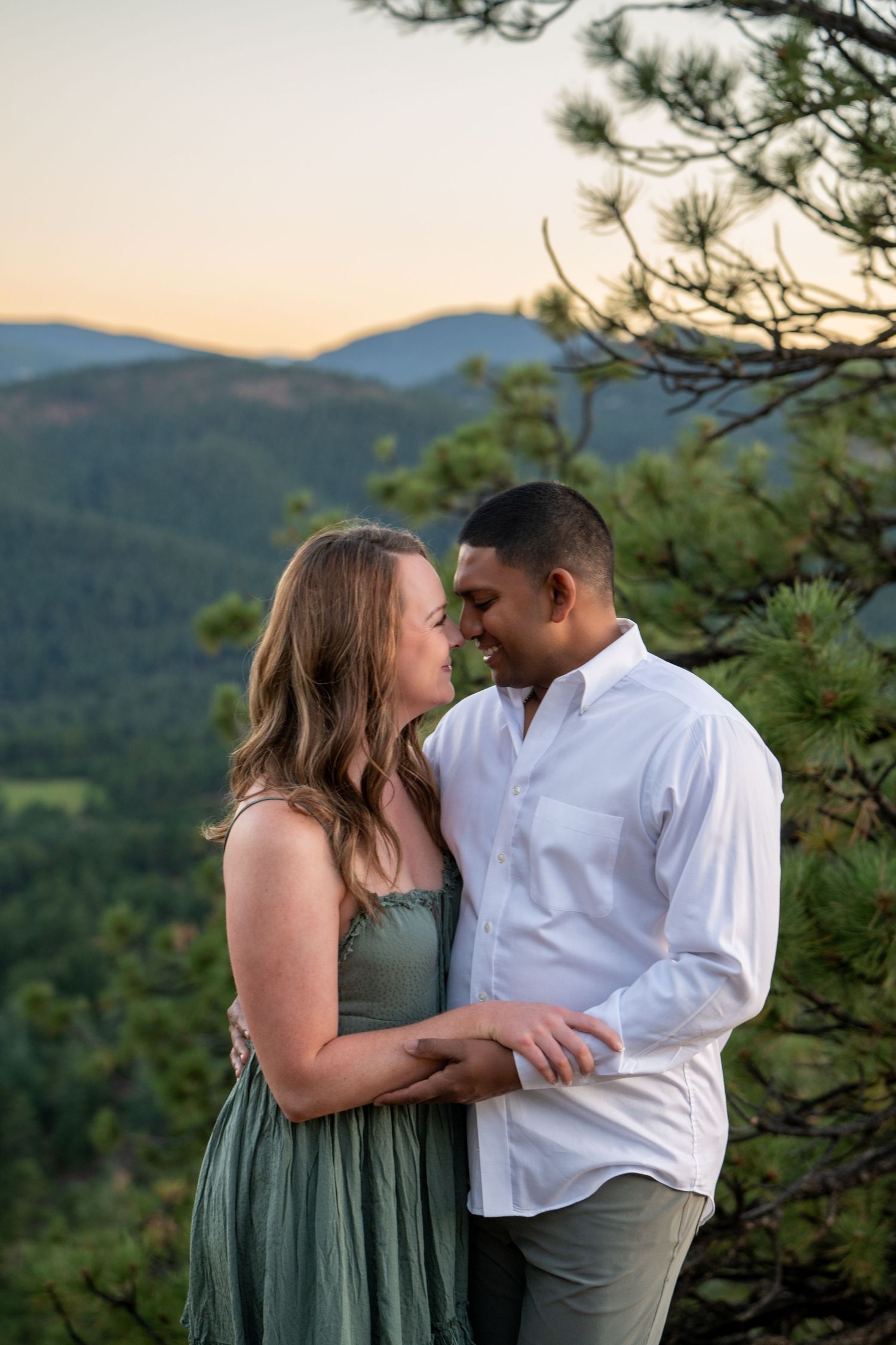 Romantic couple shares intimate moment on mountain overlook during sunset.