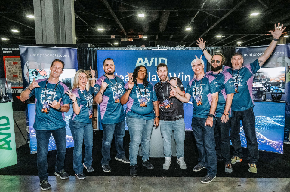 Team members in blue shirts posing together at tech conference booth with raised hands.