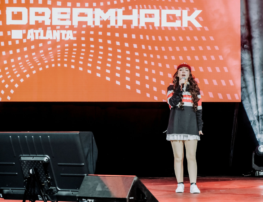 Presenter standing on stage with orange Dreamhack backdrop at gaming convention.