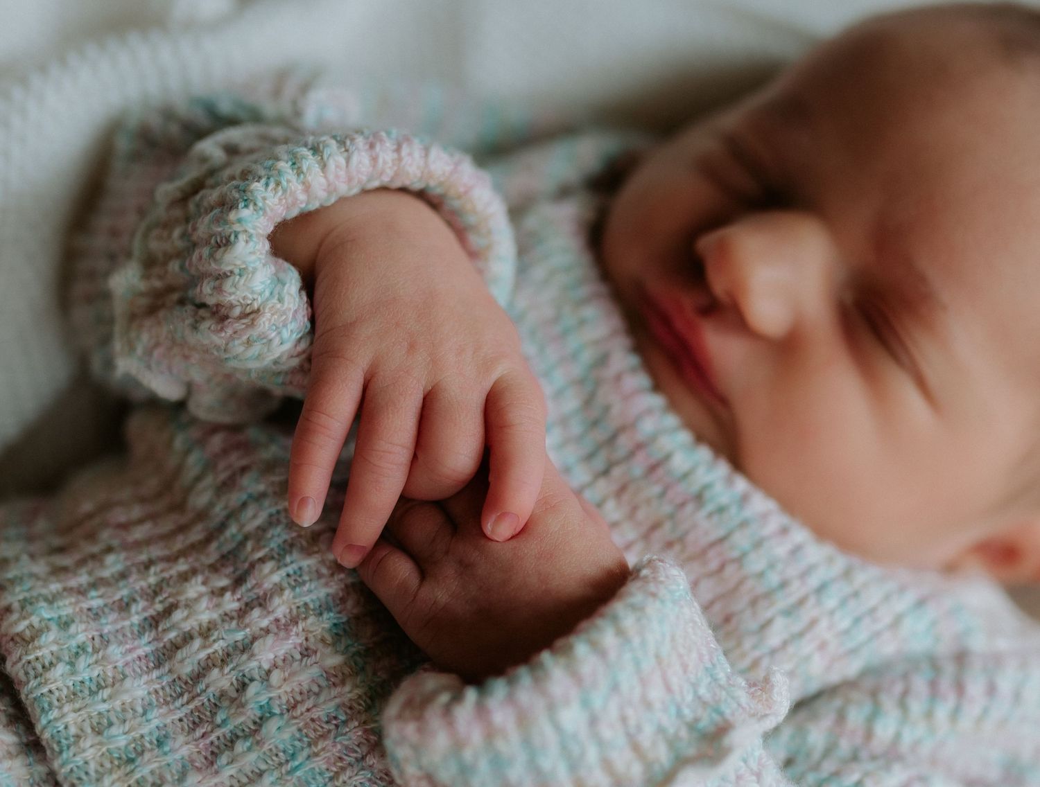 A close-up view of a newborn baby's tiny hand grasping against a soft knitted blanket in muted tones.