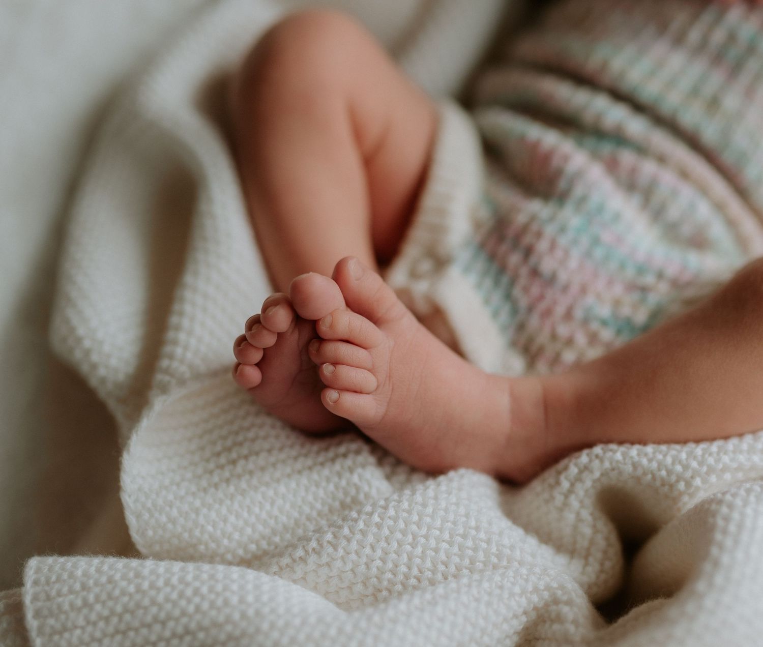 Close-up details of tiny newborn feet and hands wrapped in cozy white knit blanket.