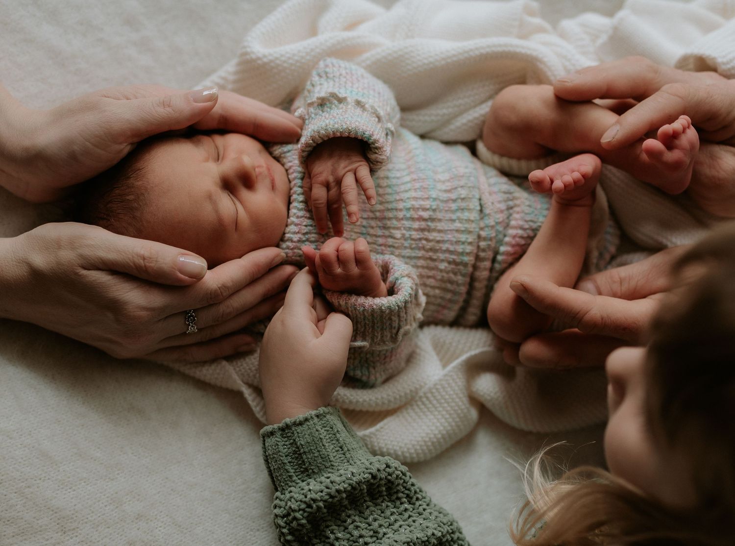 Gentle hands holding and caressing newborn baby's tiny fingers and toes.