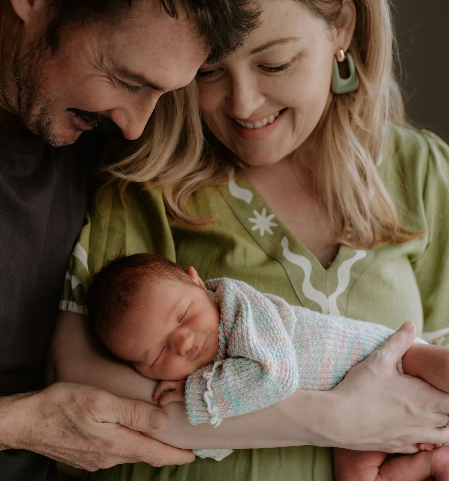 Parents lovingly gazing at their newborn baby wrapped in soft white blankets.