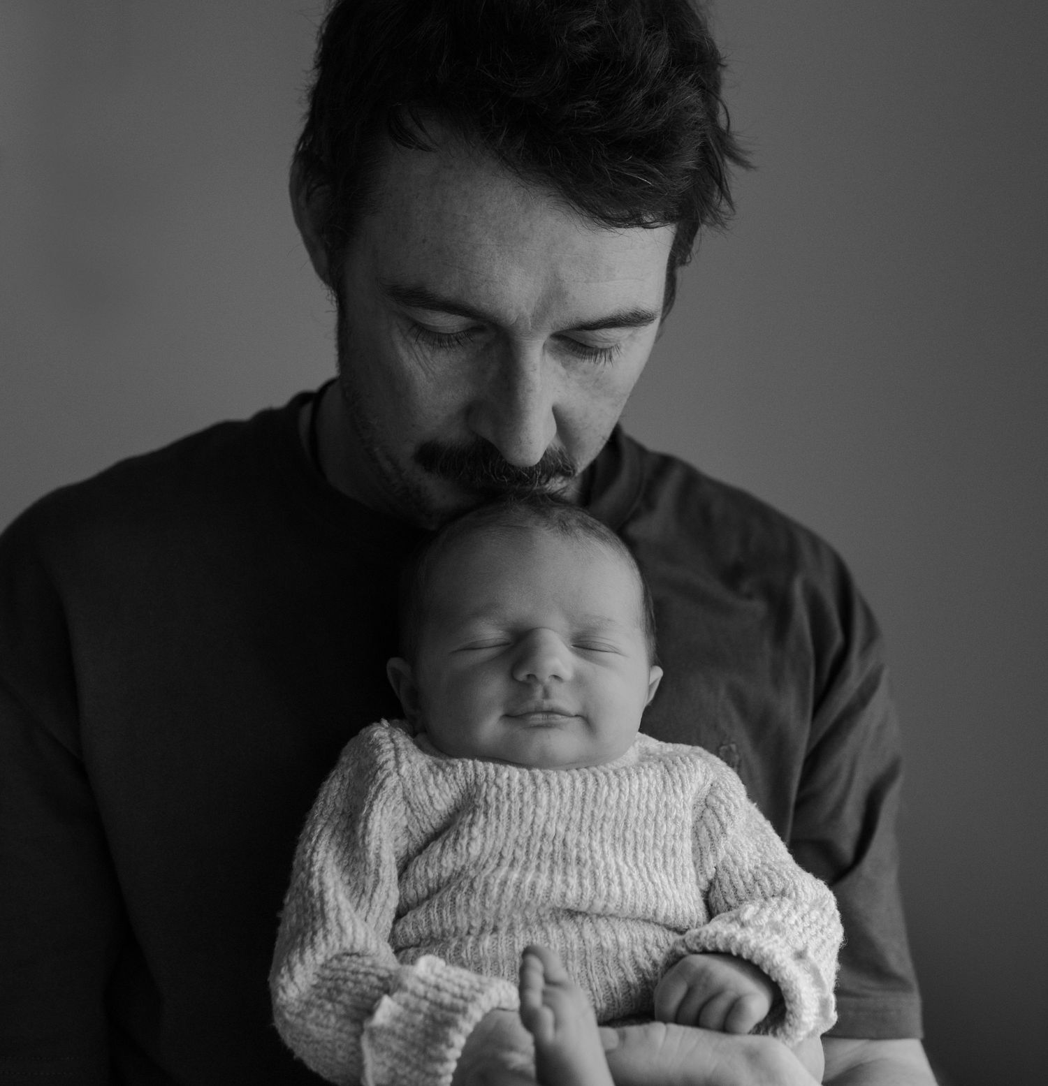 Black and white portrait series of parent bonding with sleeping newborn in knit sweater.