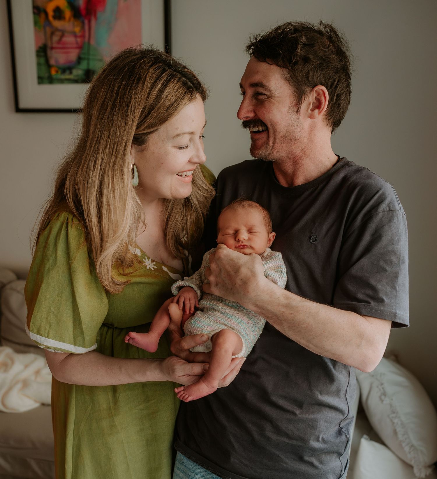 Couple in grey and green share tender moments with their newborn baby in a series of intimate indoor portraits.
