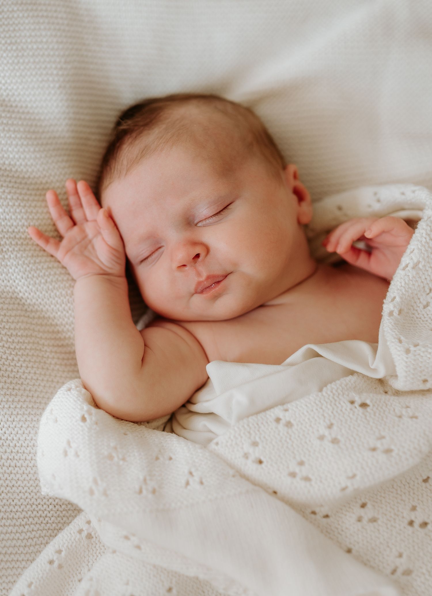 Sleeping newborn baby wrapped in white textured blanket on soft white bedding.