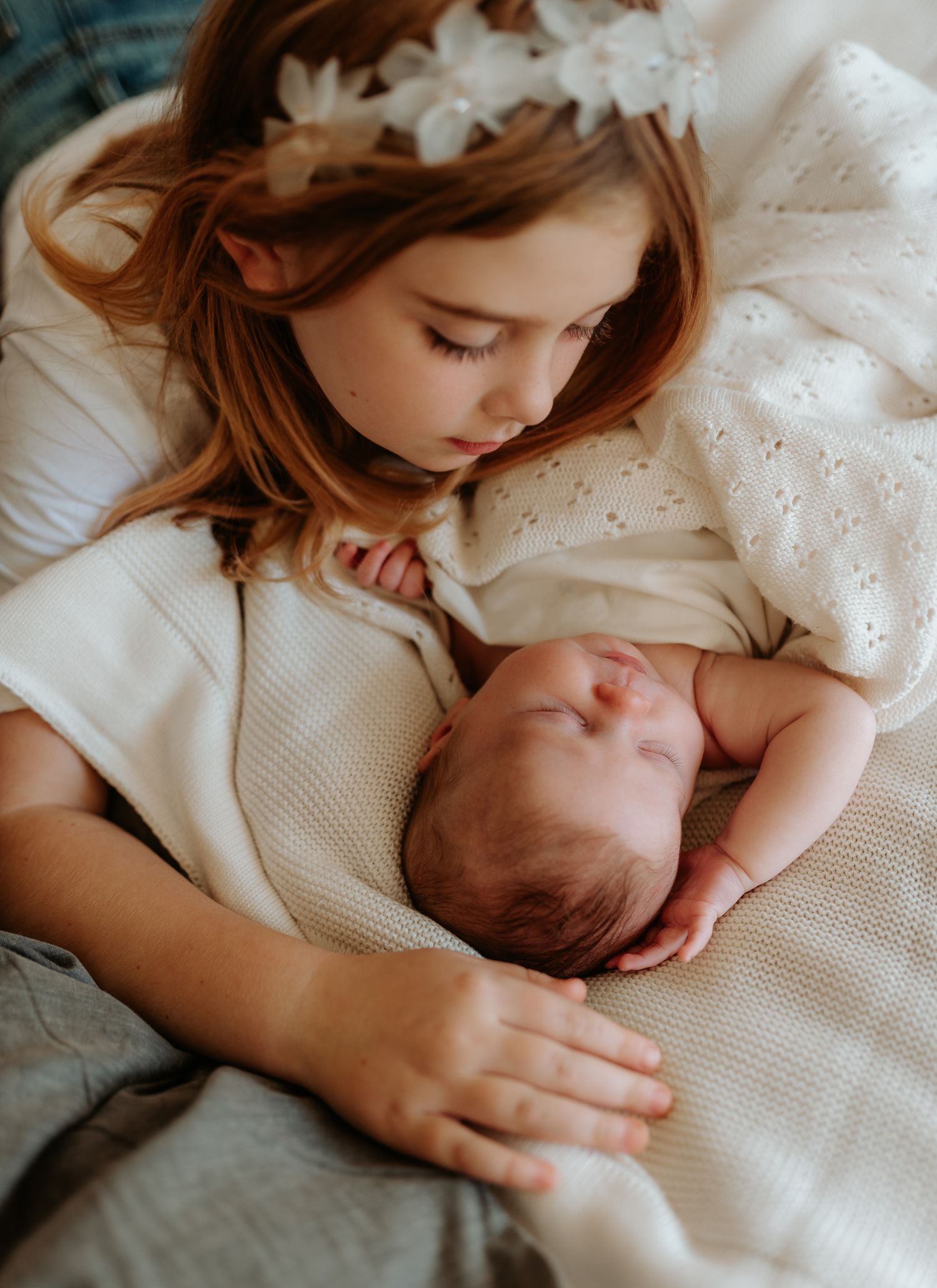 Siblings bonding moment on white bedding with soft natural light.