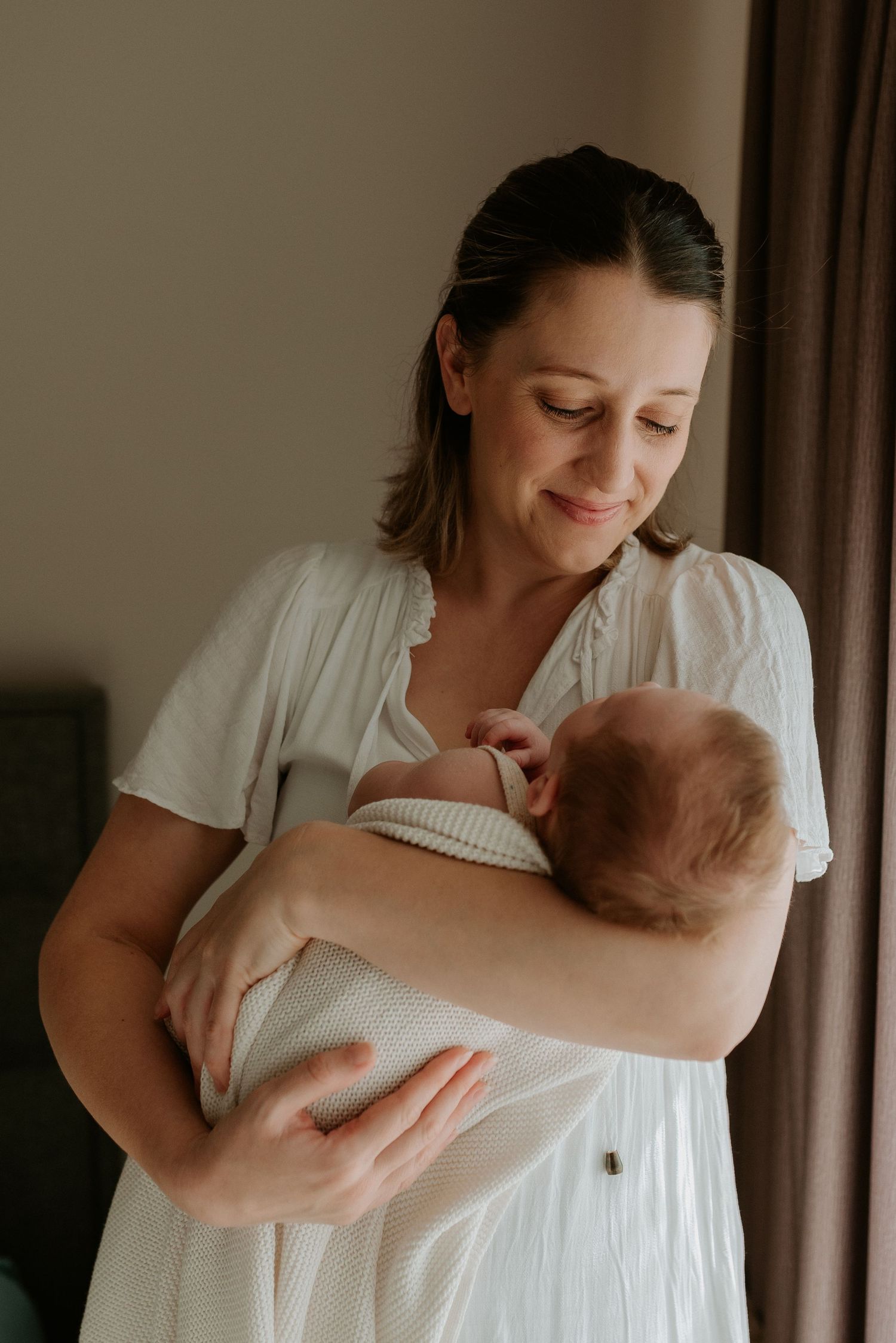 Gentle moments in white clothing with a newborn in natural window light.