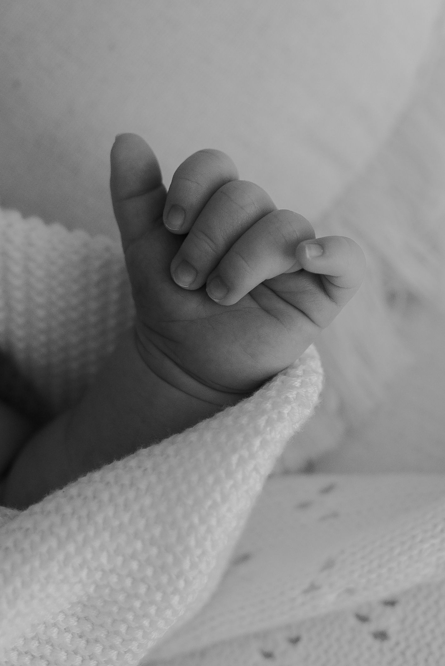 Close-up details of tiny baby hands grasping a white knitted blanket.