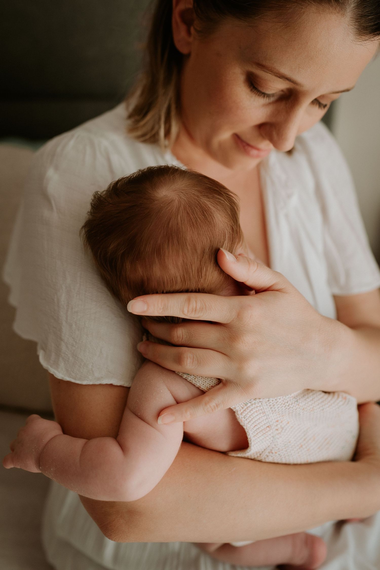 Tender embraces with a newborn wearing white against a neutral background.