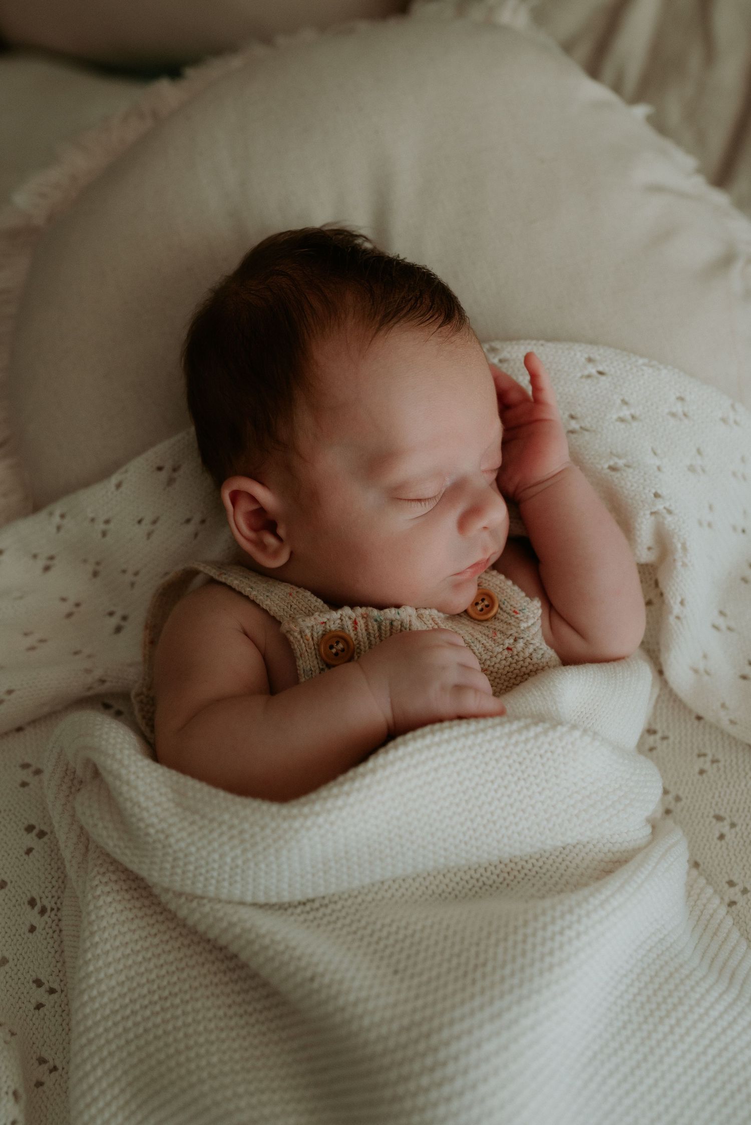 Peaceful sleeping newborn wrapped in soft white knitted blanket on textured bedding.
