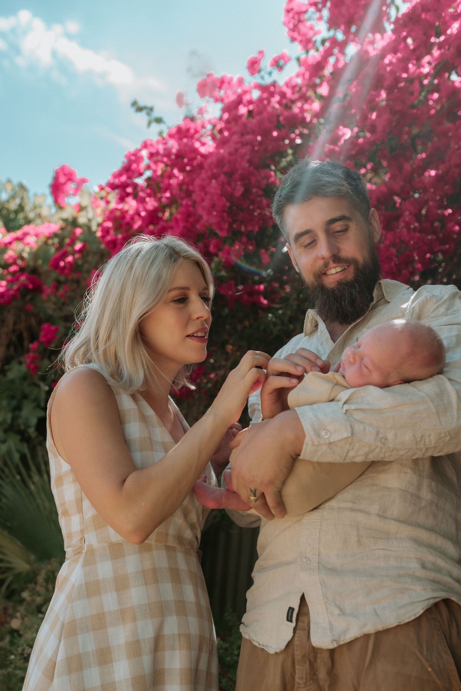 Family moment captured outdoors with vibrant pink bougainvillea flowers in background.