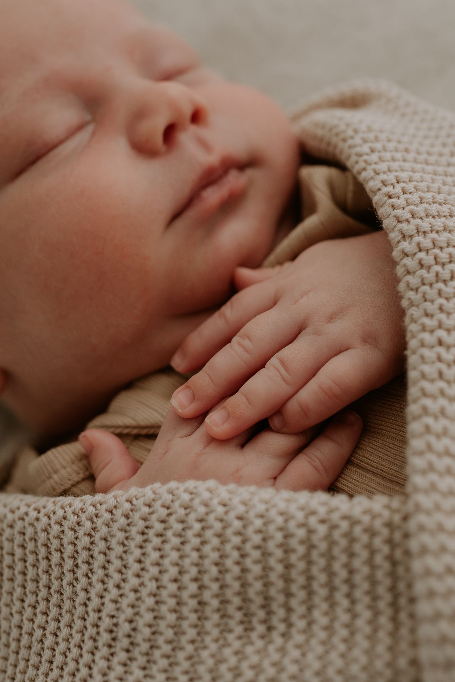 Delicate baby hands resting on a soft knitted cream-colored blanket.