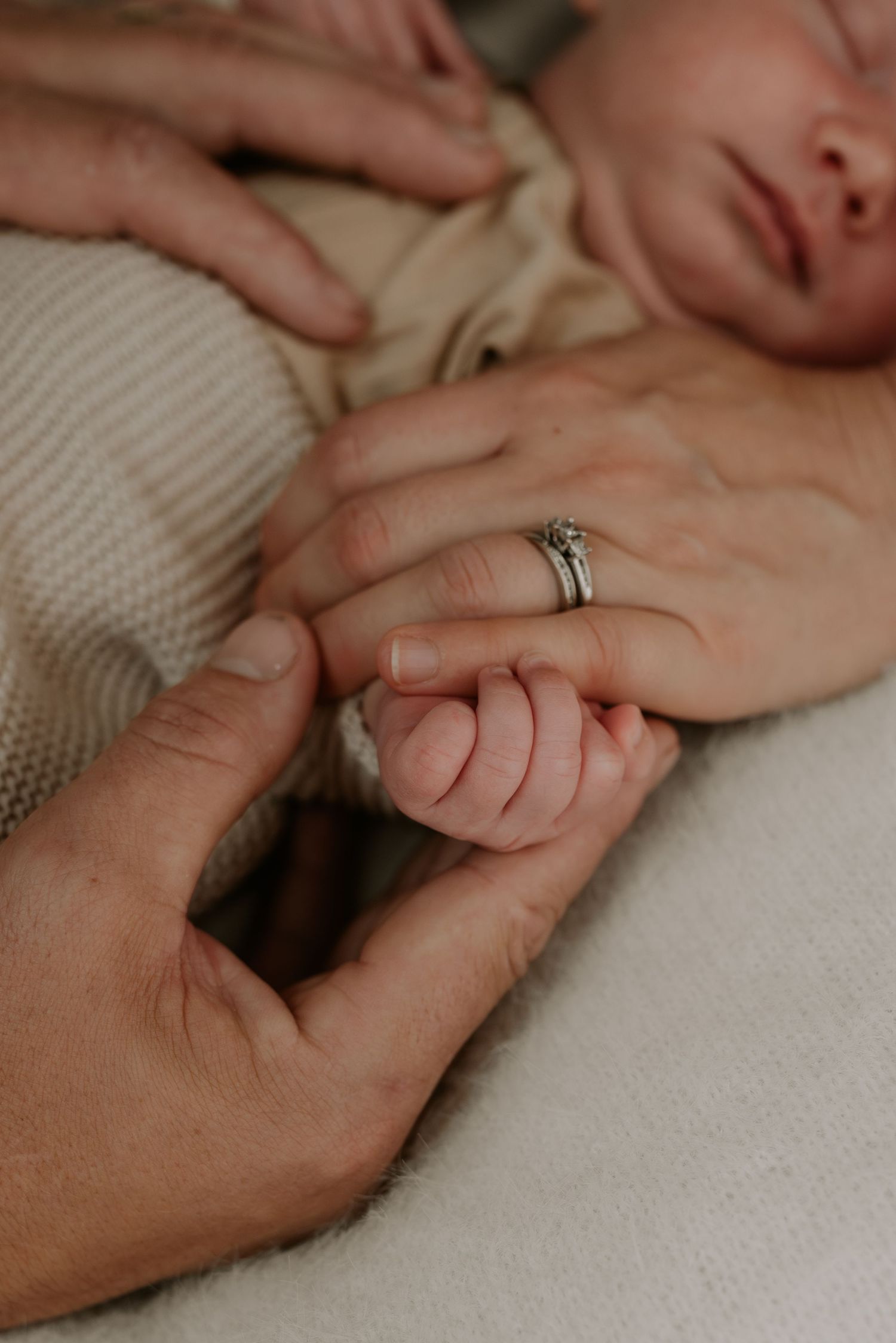 Close-up view of tiny baby fingers grasping an adult hand with a wedding ring.