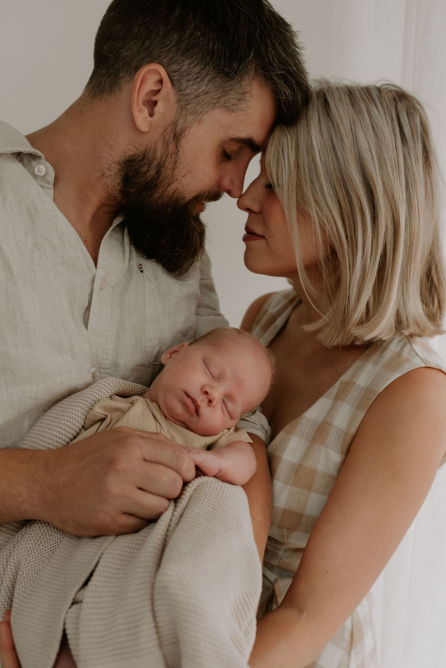 Tender family moment captured in soft natural light against white wall.