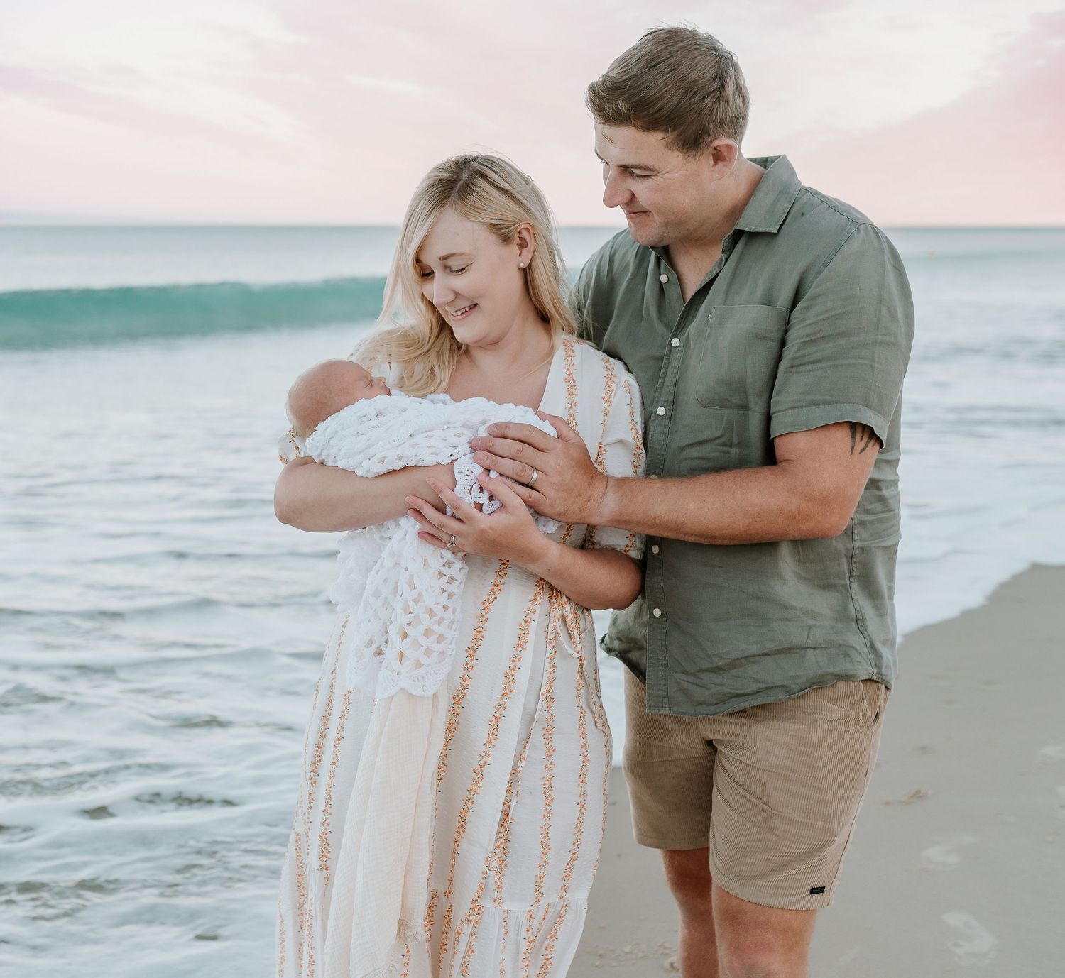 Family enjoying tender moments together on a peaceful beach at sunset.