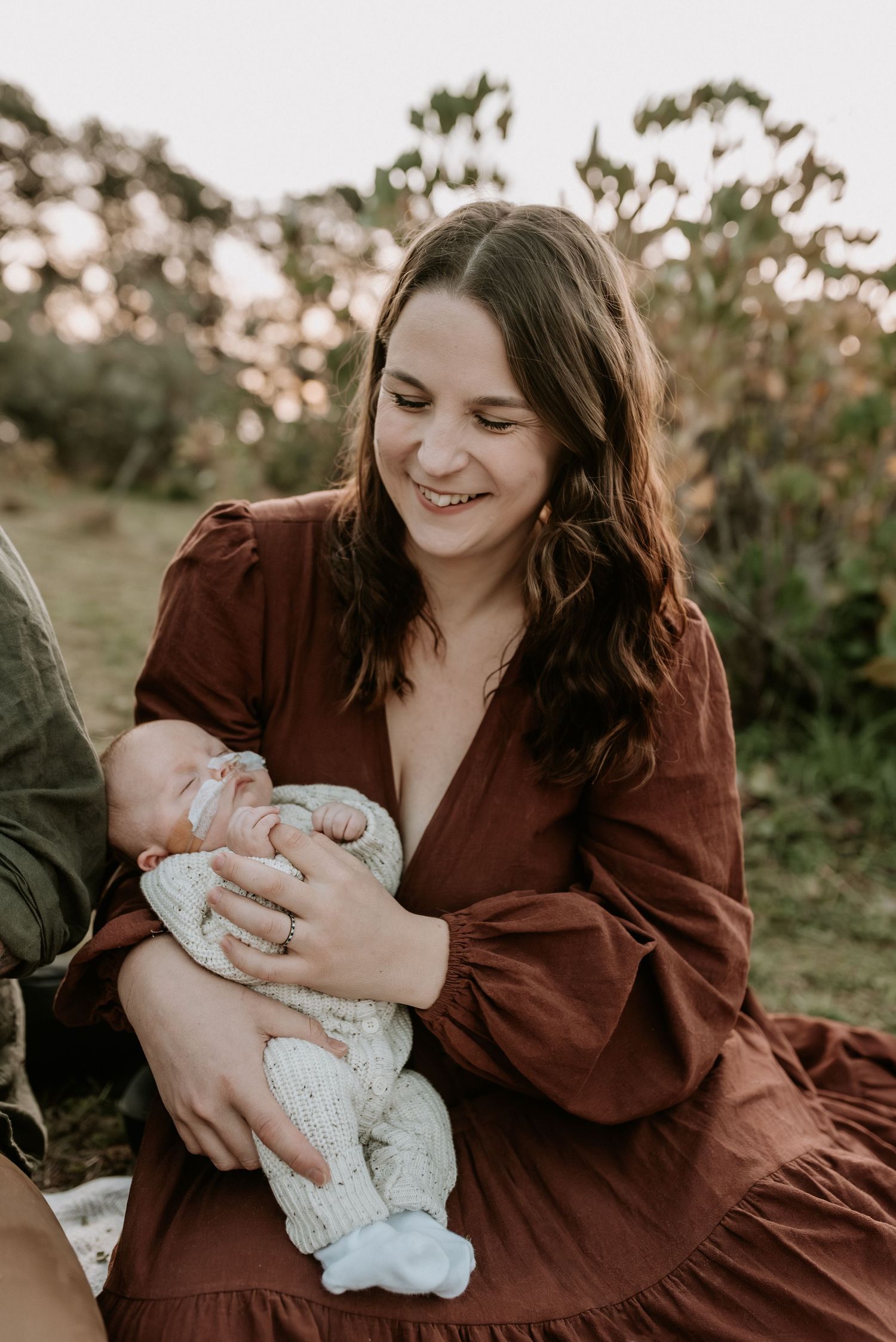 Outdoor family photoshoot in a natural setting with burgundy dress and white baby outfit.