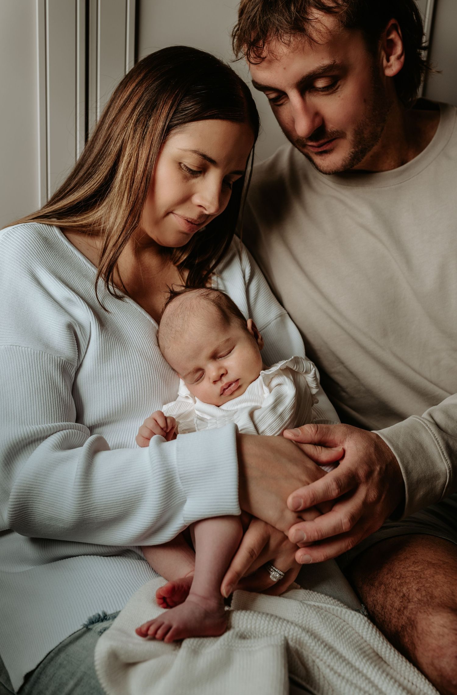 Tender family moments captured in moody lighting against grey walls.