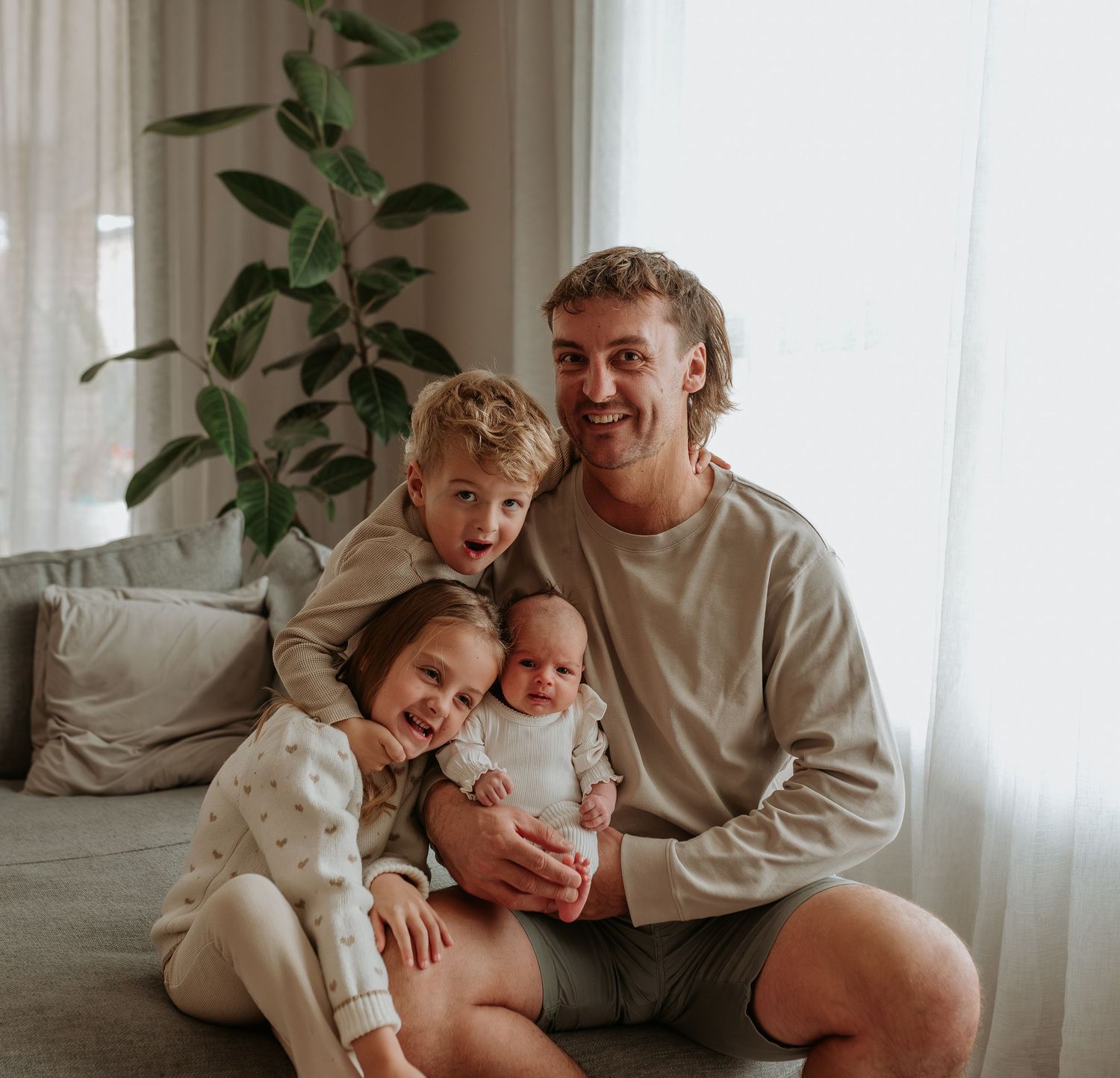 Joyful family moments captured on grey couch with natural window lighting.