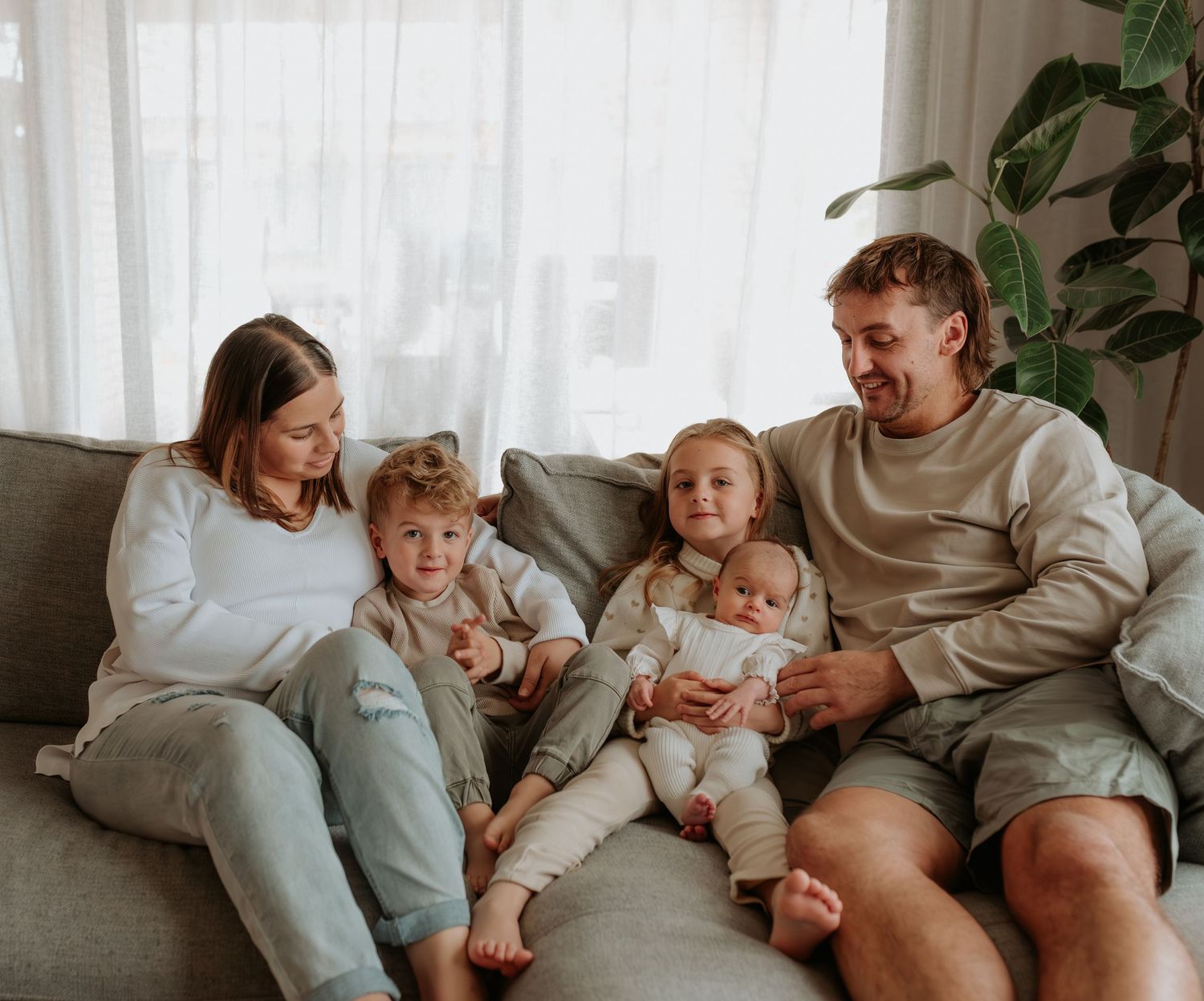 Casual family moment on grey couch with natural window lighting and indoor plants.