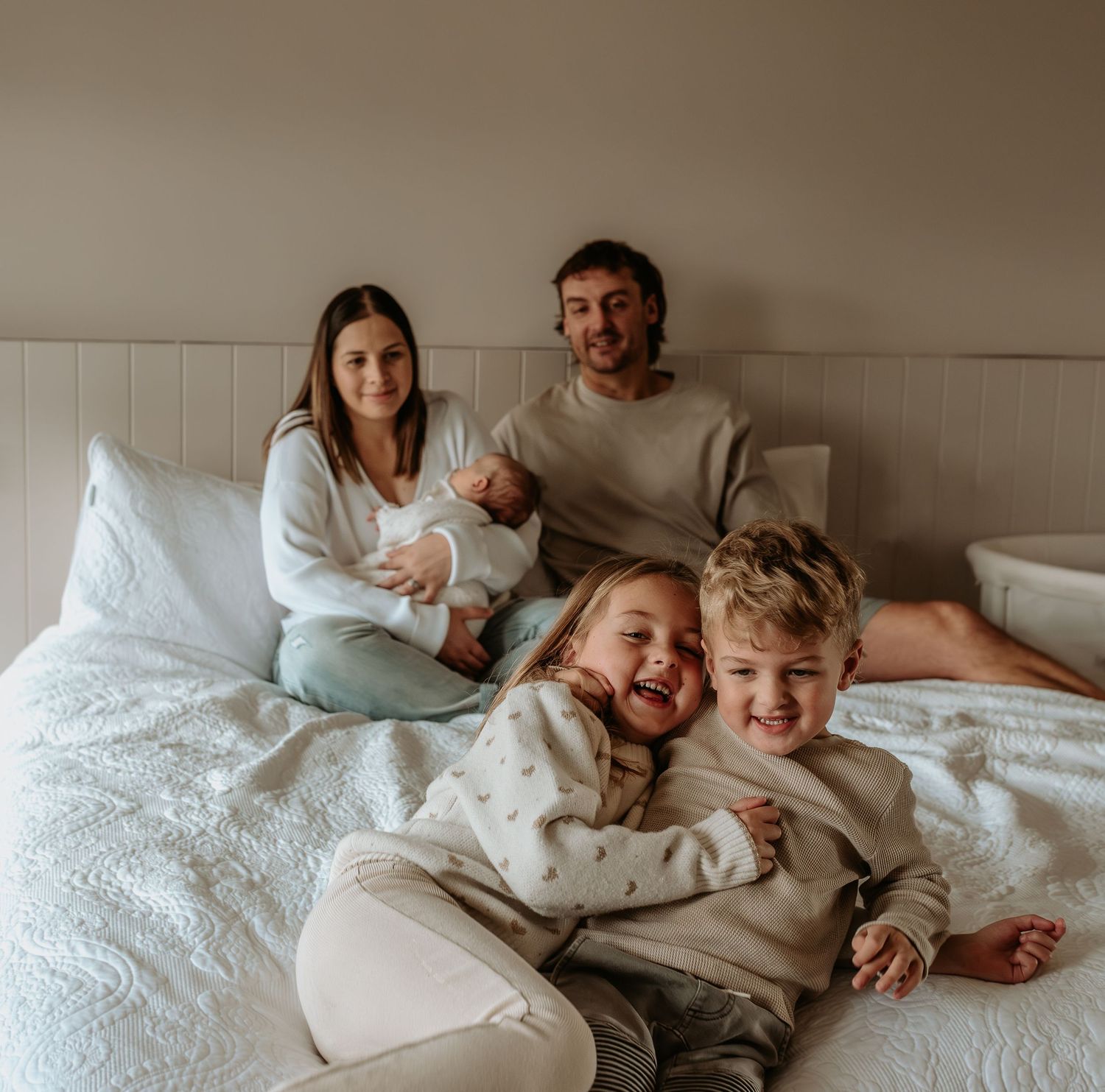 Family lying together on white bedding sharing intimate moments.