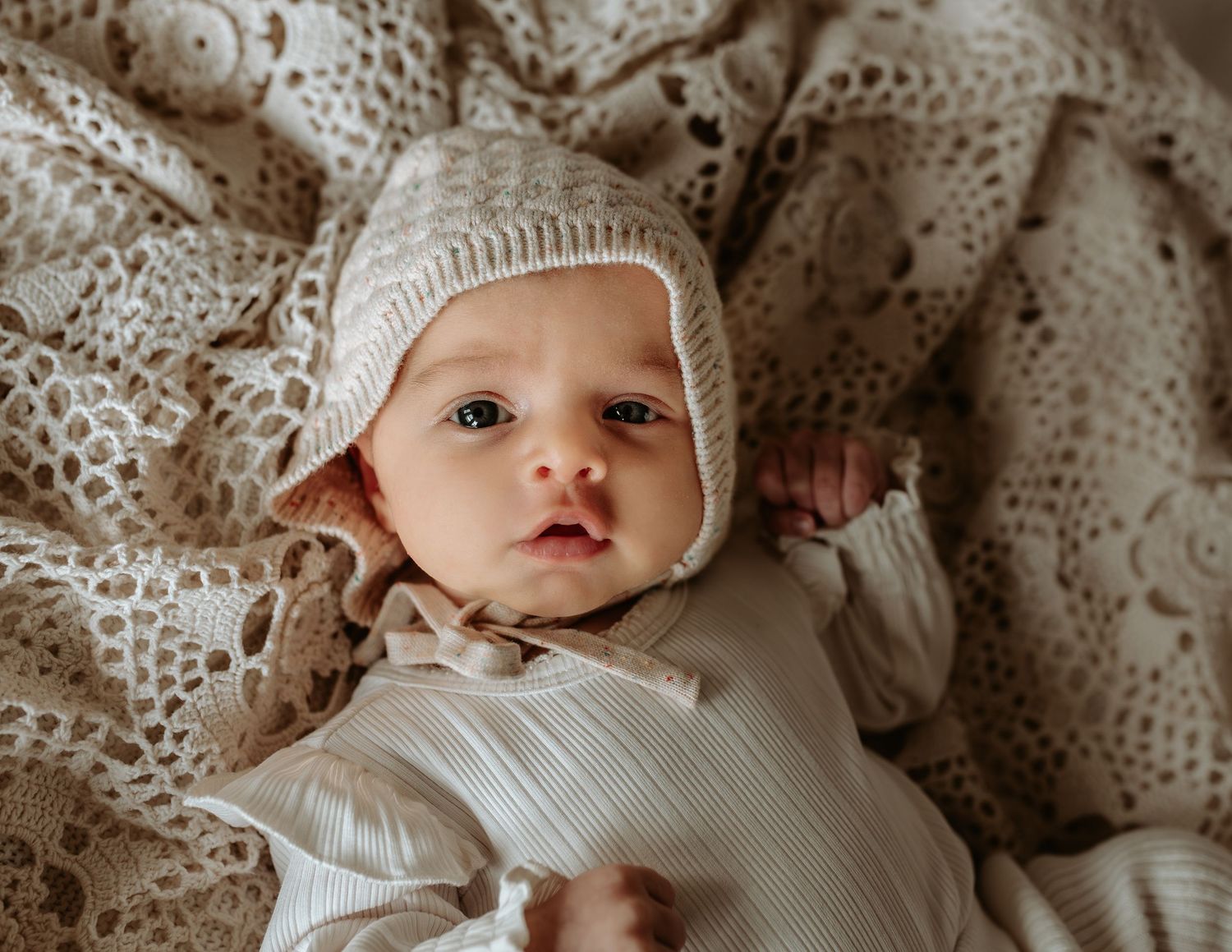 Baby wearing white bonnet photographed against delicate lace textures.