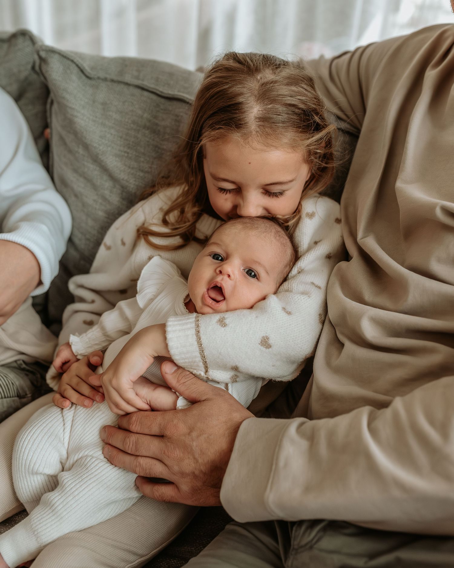 Candid family interaction series on comfortable grey couch in natural light.