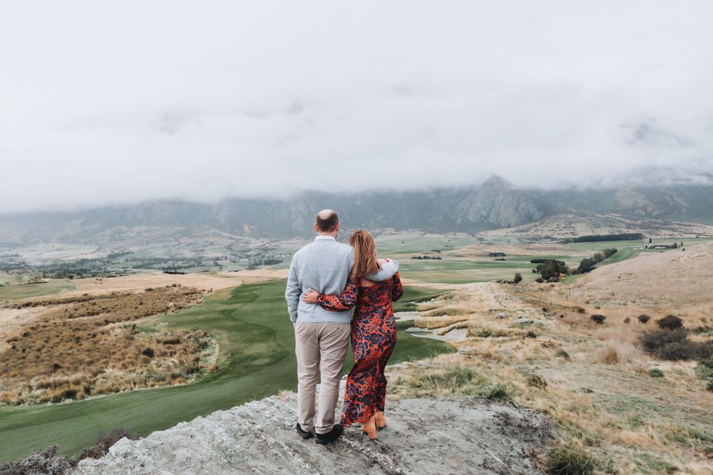 A couple admires a scenic mountain vista while standing on a rocky overlook.