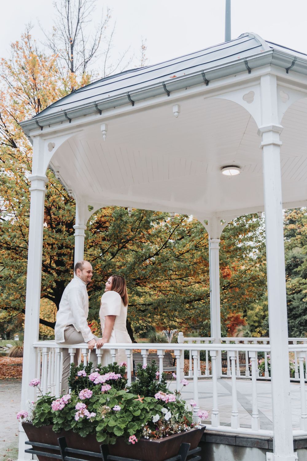 A couple shares an intimate moment on a white gazebo decorated with pink flowers.