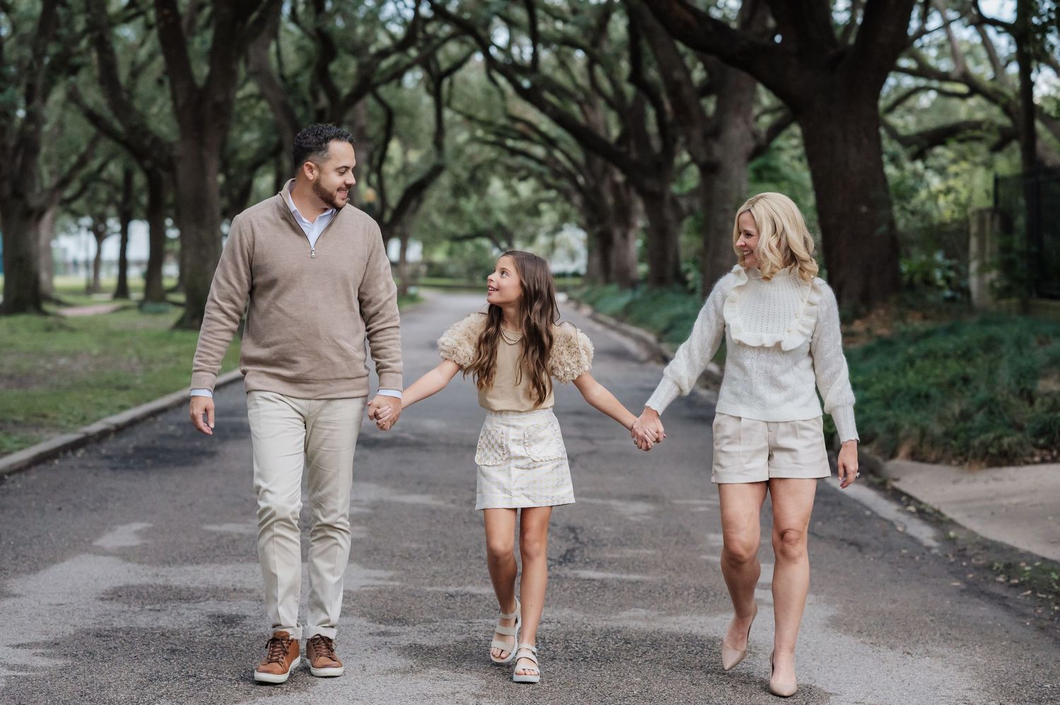 Family walking together on tree-lined path holding hands.