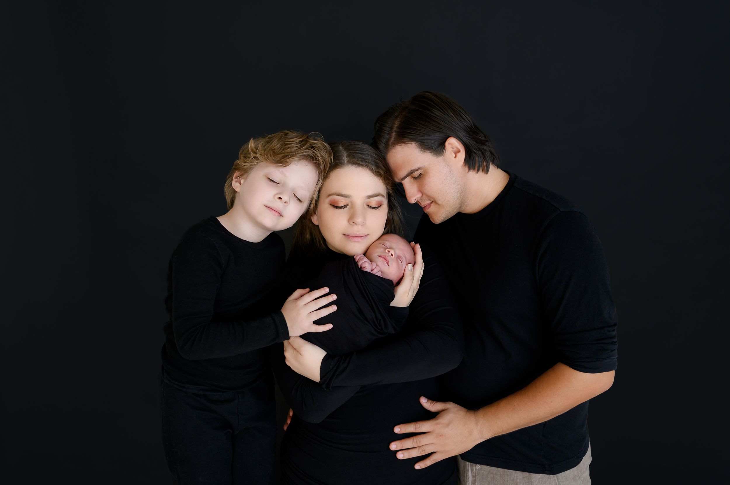 Family portrait in black clothing against dark background showing emotional connection.