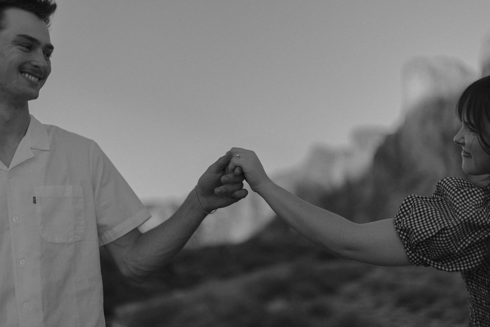 A couple holds hands against a dramatic desert landscape in black and white.