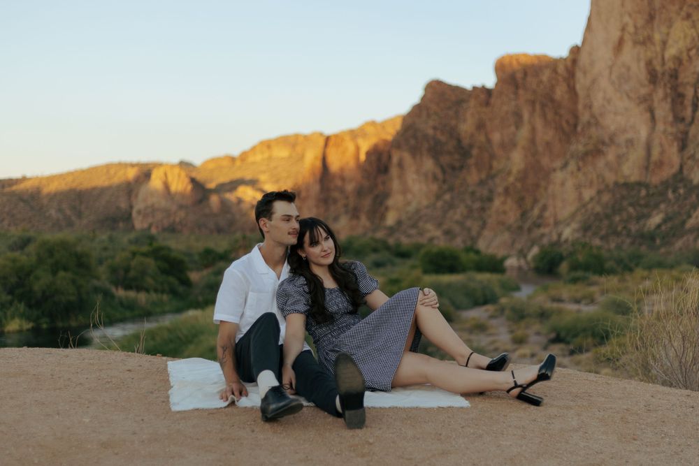 A couple relaxes on a blanket near towering desert cliffs during sunset.