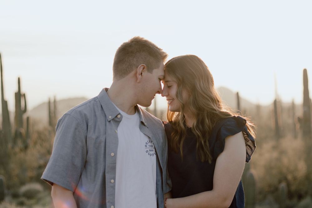 A couple shares an intimate moment against a desert backdrop with saguaro cacti at sunset.