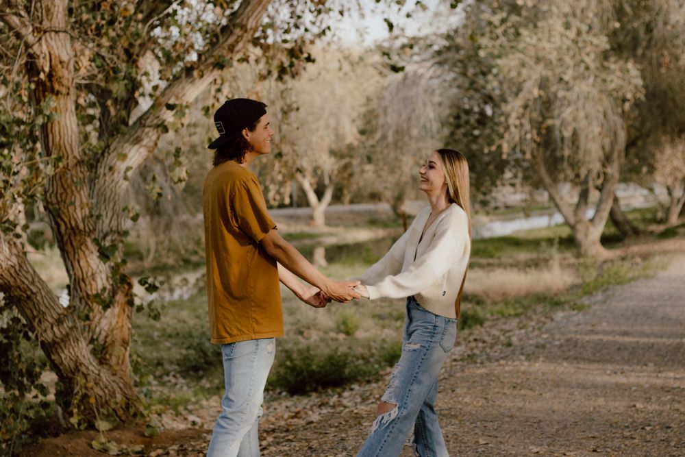 A couple holding hands while standing on a tree-lined path during golden hour.