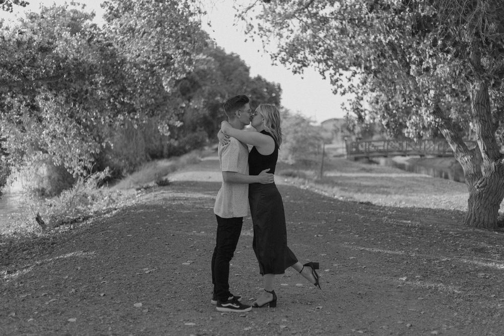 Romantic couple poses in black and white under tree branches at sunset.