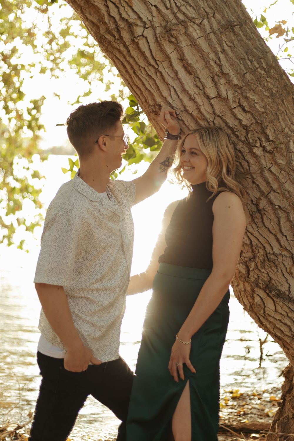 Tender couple moment captured beneath sunlit tree branches.