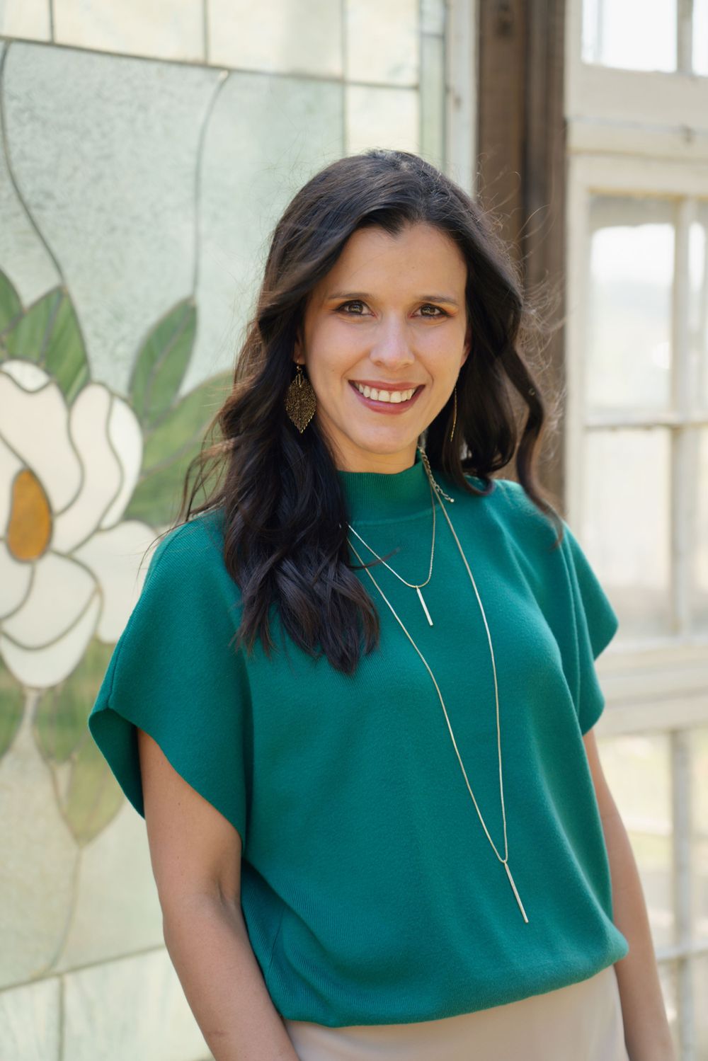 A person in a teal top poses confidently against a wall with painted magnolia flowers.