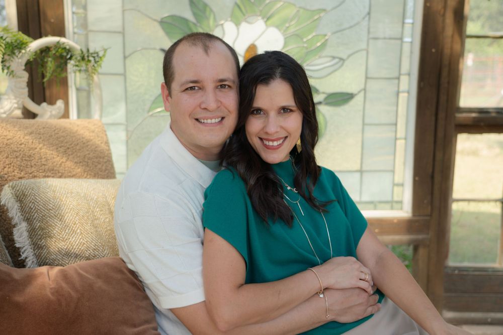 A couple smiles warmly while embracing in front of a decorative wall with painted magnolia flowers.