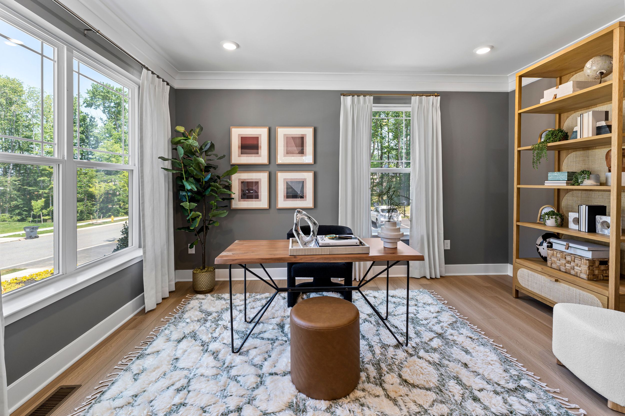 Modern home office with large windows, gray walls, and built-in wooden shelving.