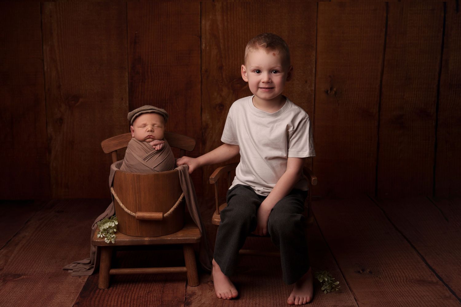 Young barefoot child sitting on wooden chair against dark wood panel wall.