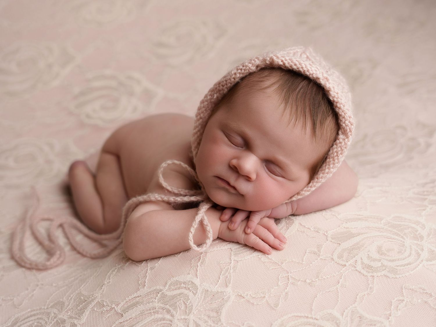 Peaceful newborn baby sleeping in knit bonnet on textured backdrop.