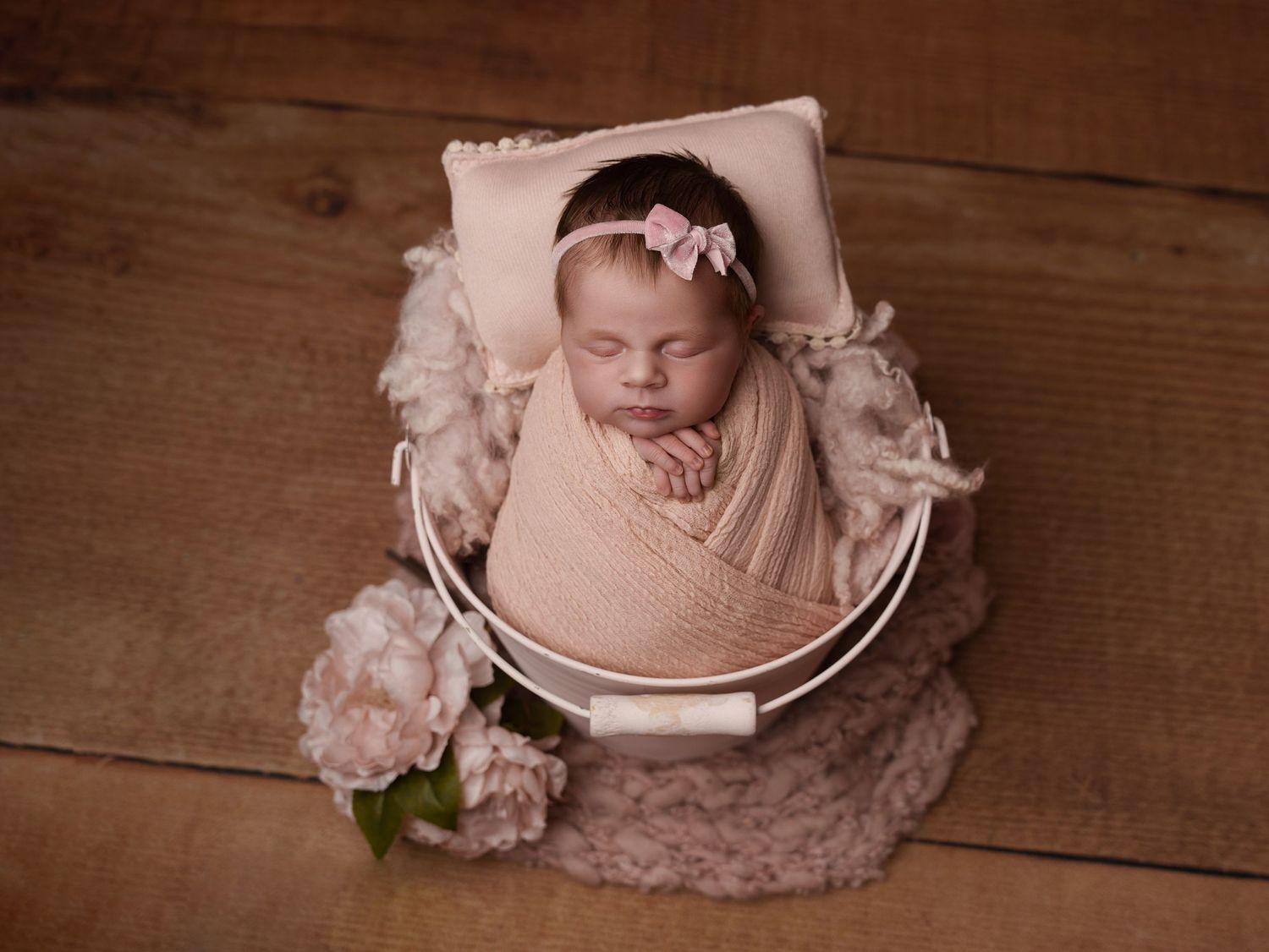 Newborn wrapped in pink swaddle sleeping in white bowl with floral accents.