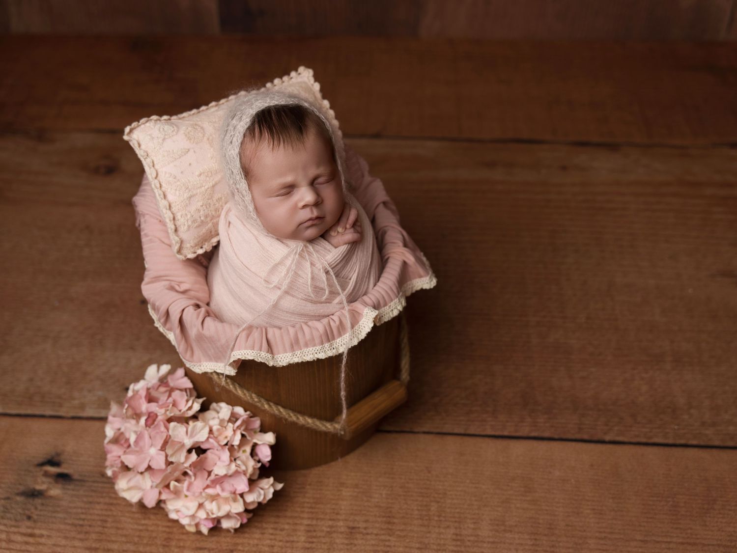 Baby rests in vintage box with pink hydrangeas on wooden floor.