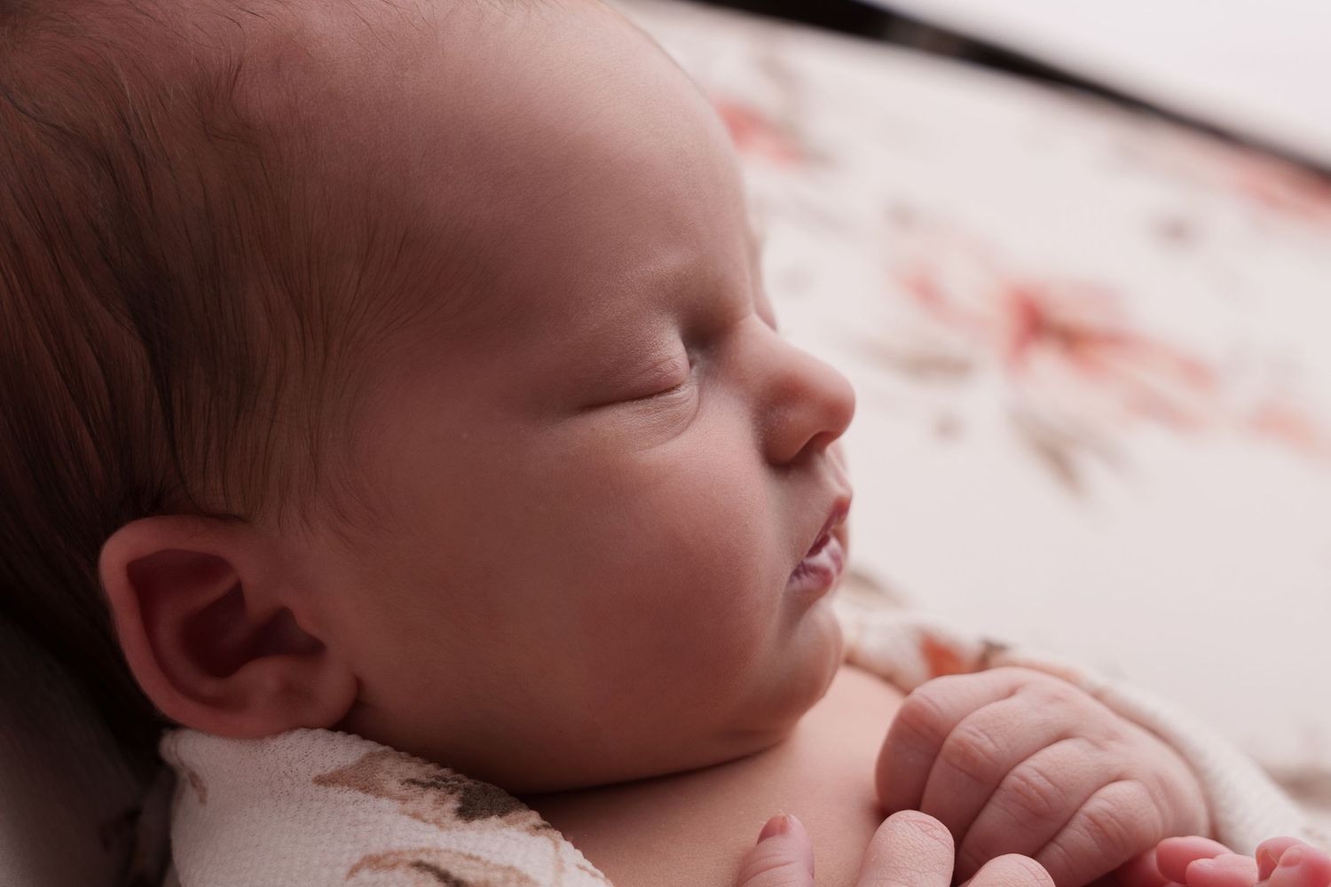 Peaceful newborn sleeps on floral patterned fabric in gentle natural light.
